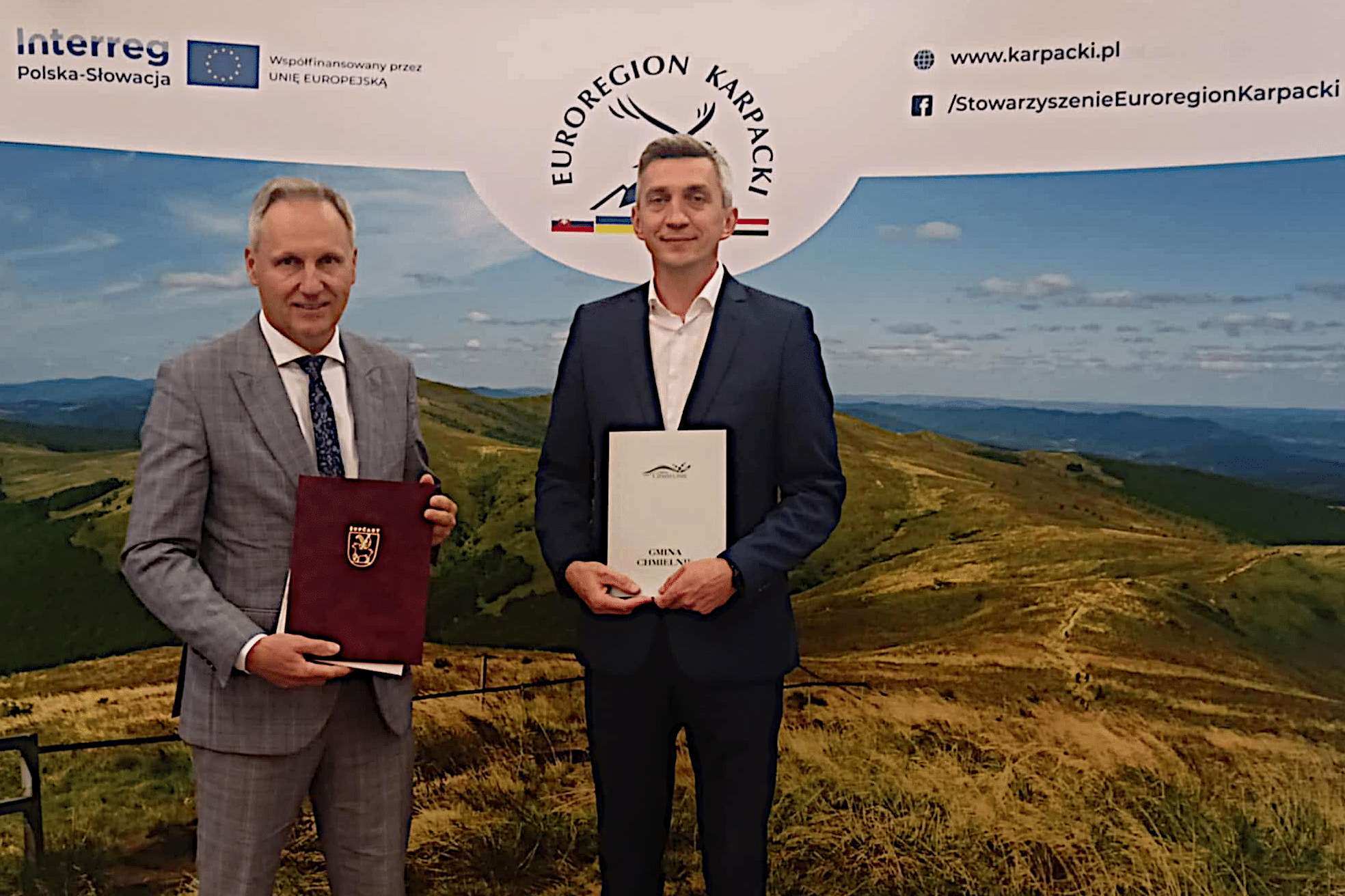 Zdjęcie przedstawia wójta Gminy Chmielnik po lewej oraz starostę Zupčan na Słowacji po prawej. Obaj mężczyźni stoją przed banerem Euroregionu Karpackiego i trzymają dokumenty związane z podpisanym porozumieniem.